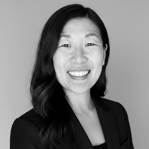 Smiling woman with long dark hair in a black blazer poses against a plain, light background.